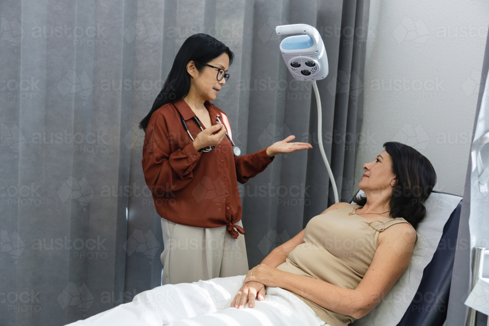 Female doctor talking to patient lying on exam bed - Australian Stock Image