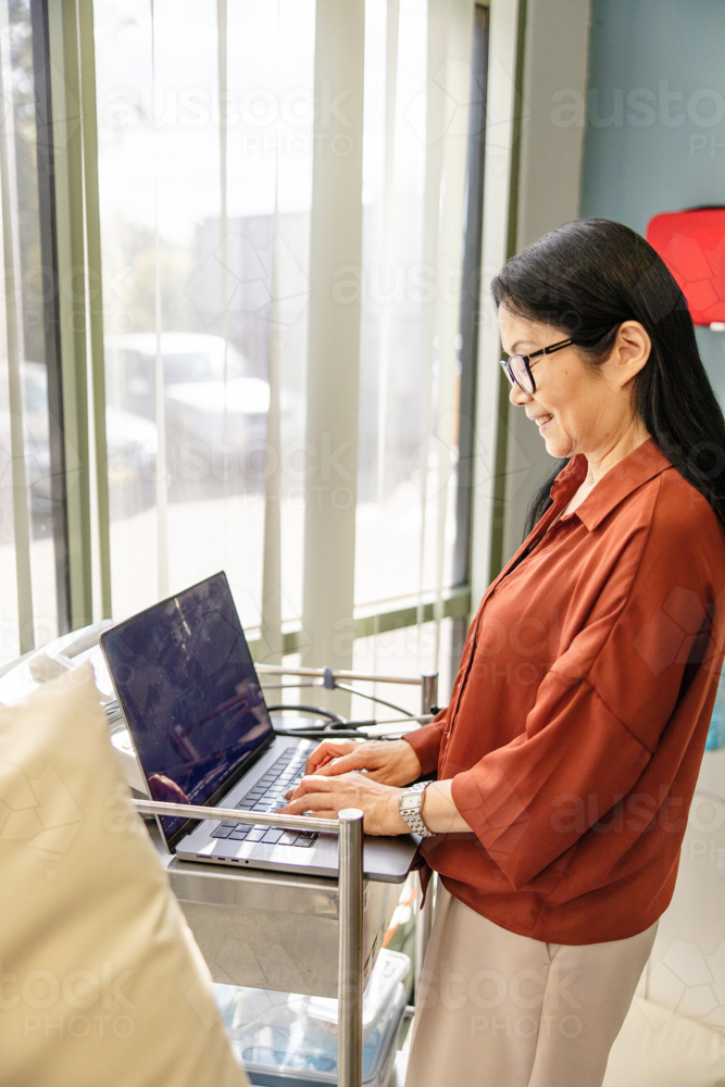 Female doctor typing on the laptop for documentation - Australian Stock Image