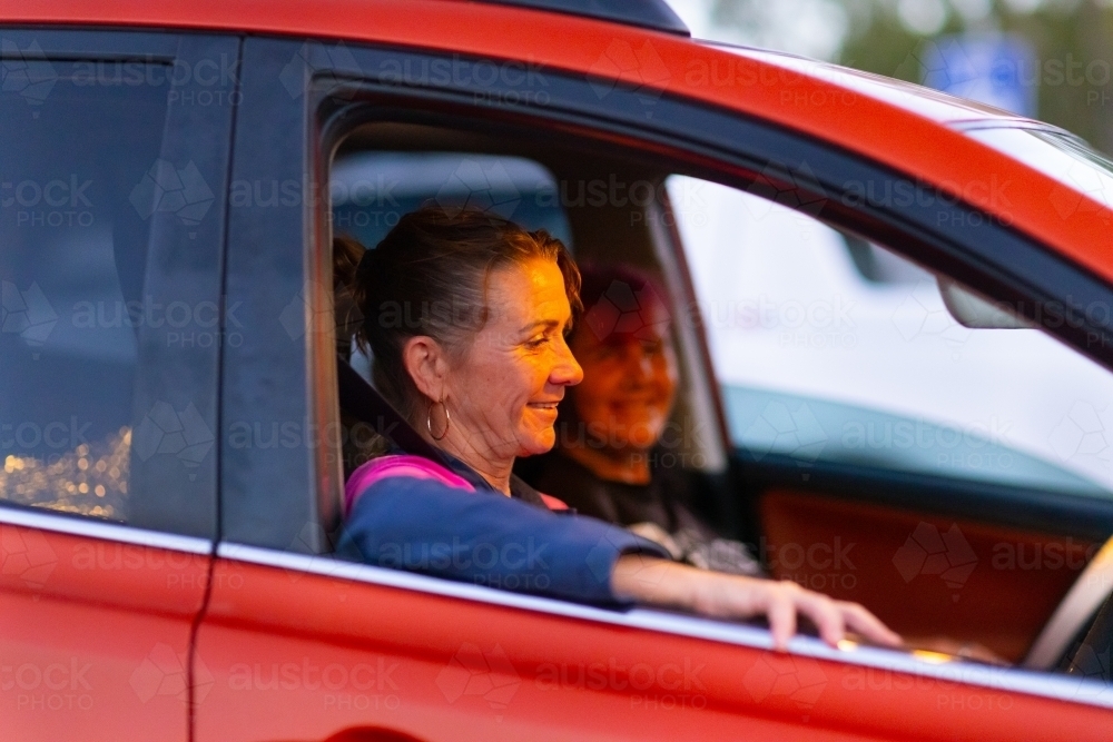 female driver of car with arm leaning out window with passenger blurred in background - Australian Stock Image