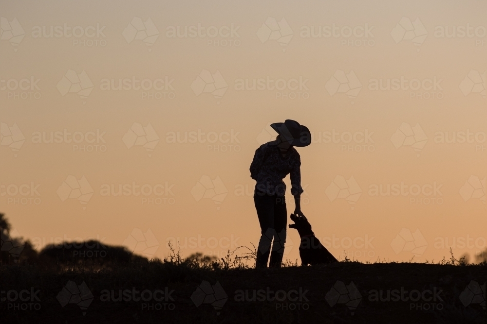 Female farmer petting dog in silhouette - Australian Stock Image