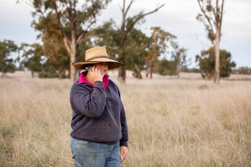 Female farmer using a mobile phone in the paddock - Australian Stock Image