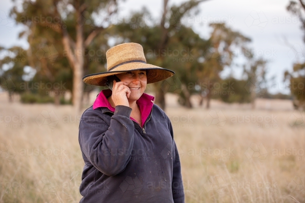 Female farmer using iphone in the paddock - Australian Stock Image