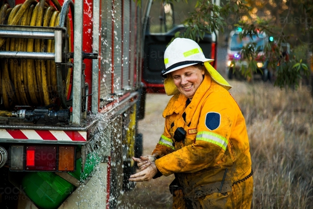 Female firefighter laughing and washing her hands beside firetruck - Australian Stock Image