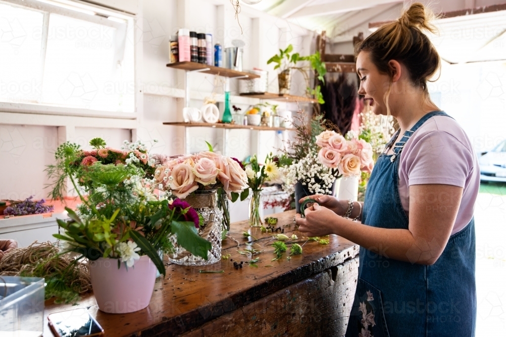 Female florist preparing wedding suit buttonholes at a work bench full of vases of flowers - Australian Stock Image