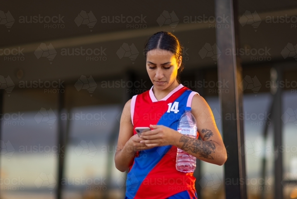 Female football player holding a water bottle and  looking at her phone - Australian Stock Image