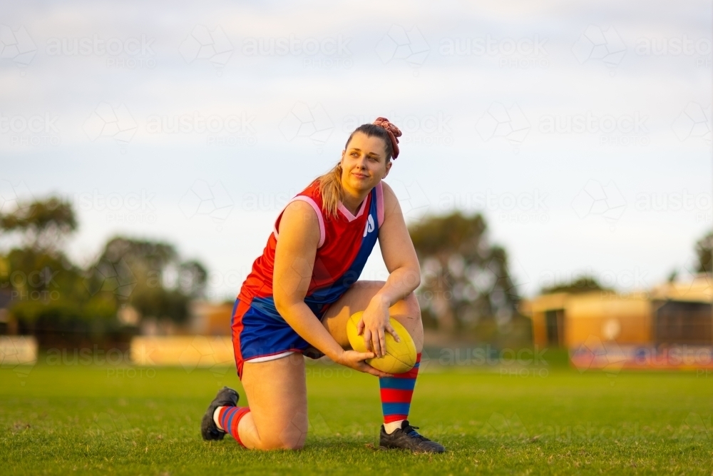 female footballer kneeling on grass on one knee with football - Australian Stock Image