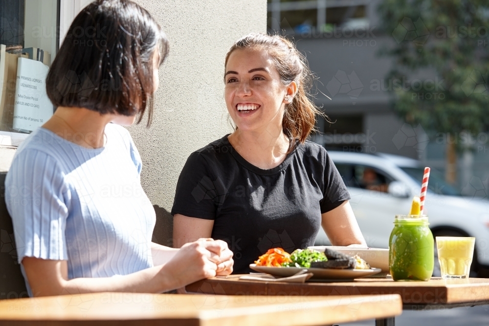 Female friends sitting outdoors at cafe in sunshine - Australian Stock Image
