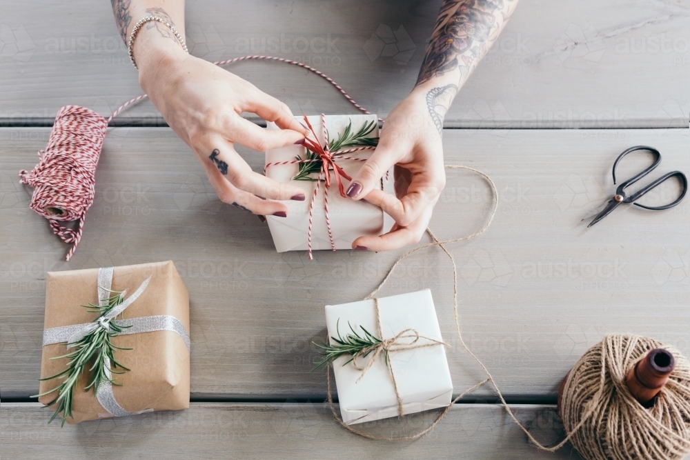Female hands tying bows on stylishly wrapped Christmas gifts - Australian Stock Image