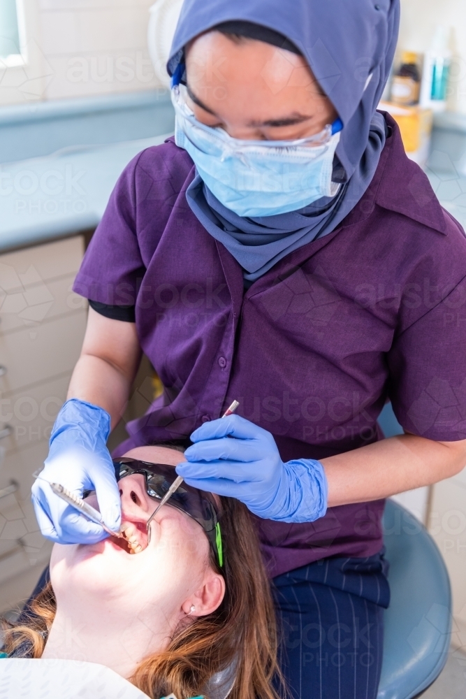 Female having teeth cleaned by dentist wearing hijab - Australian Stock Image