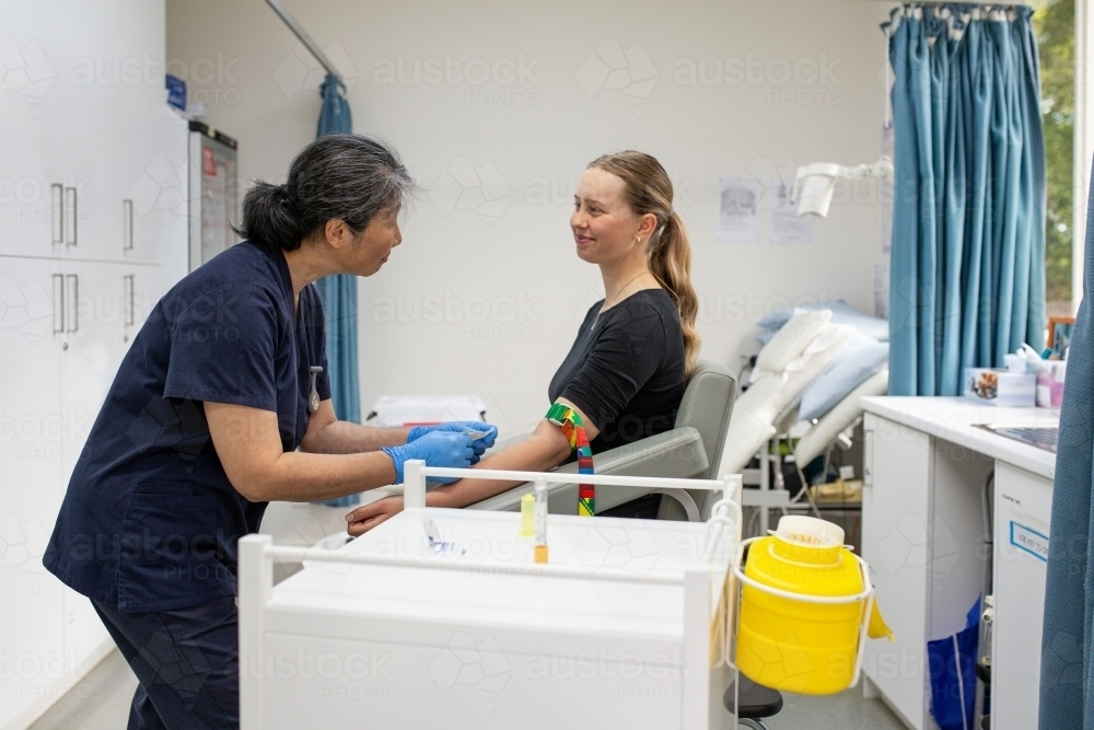 Female health care working talking to a female patient while putting tourniquet on her arm - Australian Stock Image