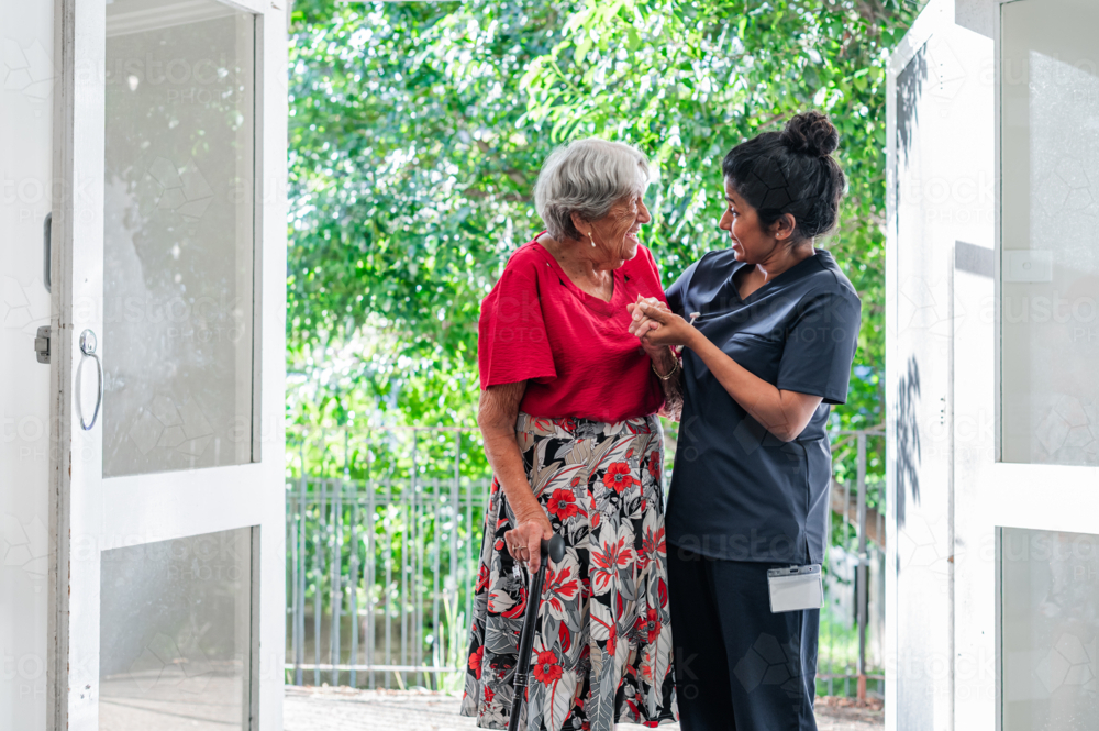 Female health caregiver assisting an elderly woman walking through the doorway - Australian Stock Image