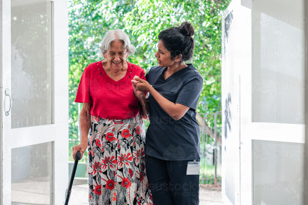 Female health caregiver assisting an elderly woman walking through the doorway - Australian Stock Image