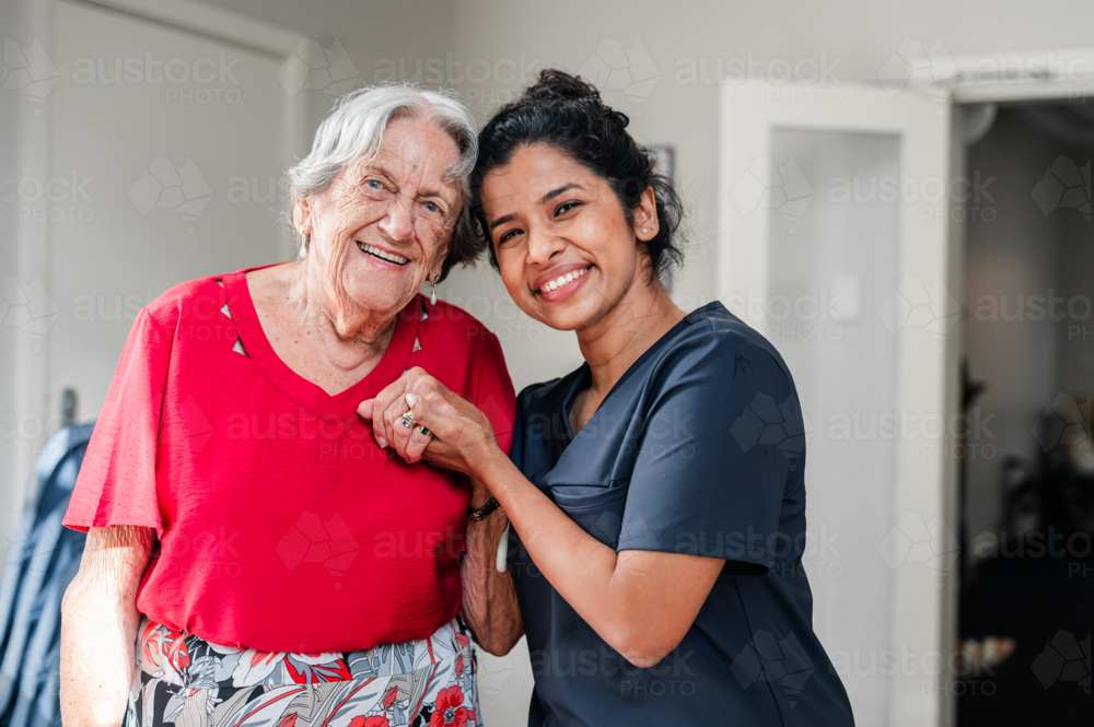 Female health caregiver assisting an elderly woman walking through the doorway - Australian Stock Image