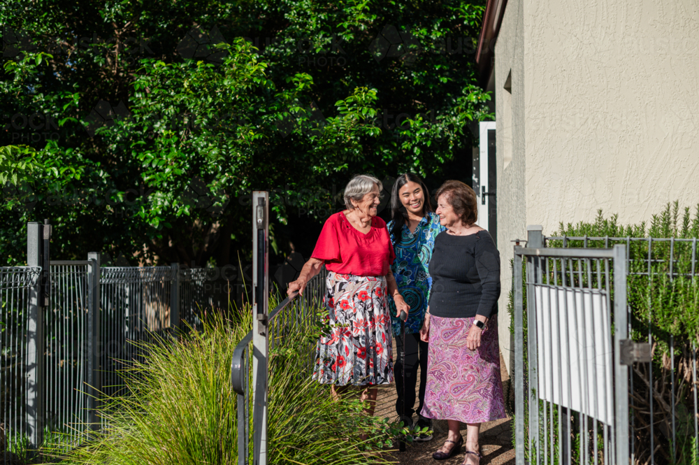 Female healthcare worker assisting two elderly women for a walk on a paved path outdoors - Australian Stock Image