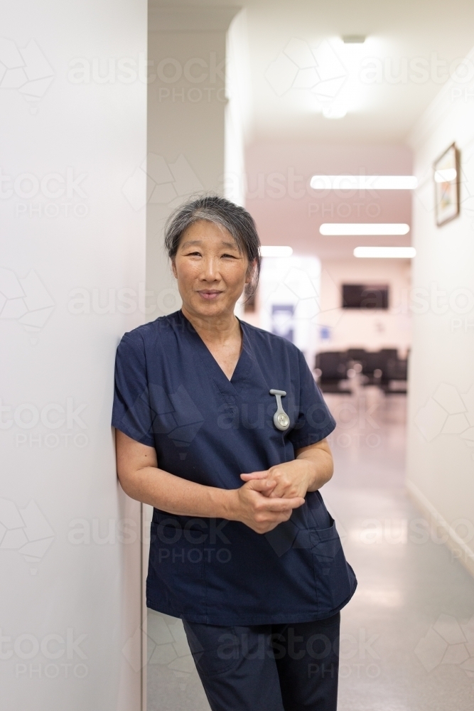 Female healthcare worker leaning on the wall smiling at the camera - Australian Stock Image