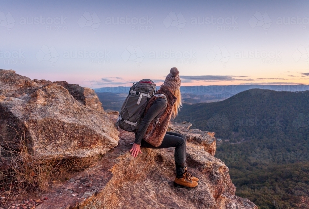 Female hiker with backpack rests on a mountain peak rocky ledge in Blue Mountains Australia  - Australian Stock Image