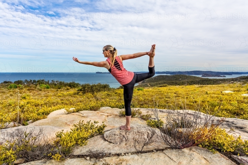 Female in outdoor coastal setting with wildflowers blooming doing yoga - Australian Stock Image