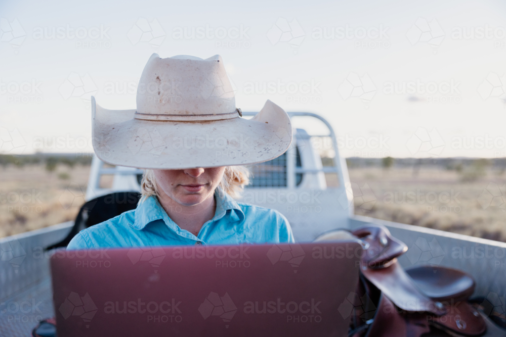 Female looking at computer outdoors with vehicle in background - Australian Stock Image
