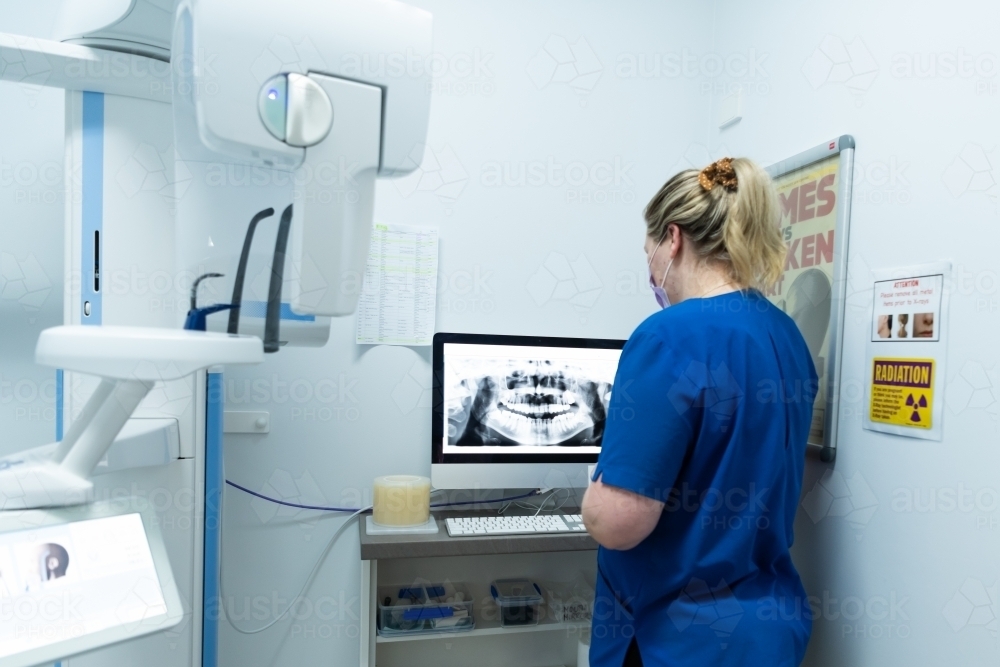 Female looking at teeth and jaw dental x-ray on monitor - Australian Stock Image