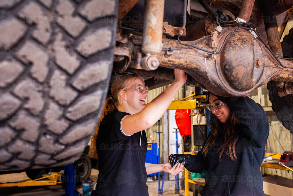 female mechanic tradeswomen working on car repair together in industrial workshop - Australian Stock Image