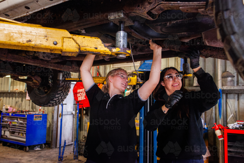 female mechanic tradeswomen working together on car repair in industrial workshop - Australian Stock Image