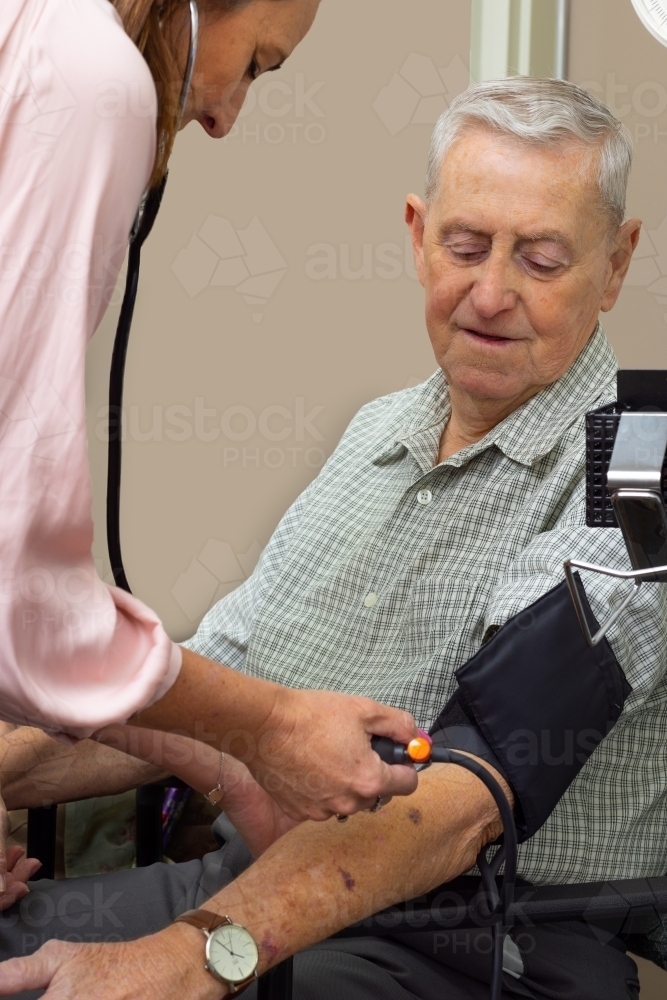 female medical professional taking blood pressure test on elderly man - Australian Stock Image
