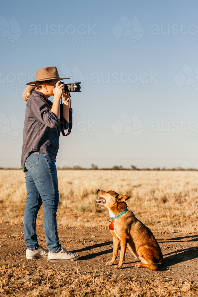 Female photographer outdoors looking through camera with dog - Australian Stock Image