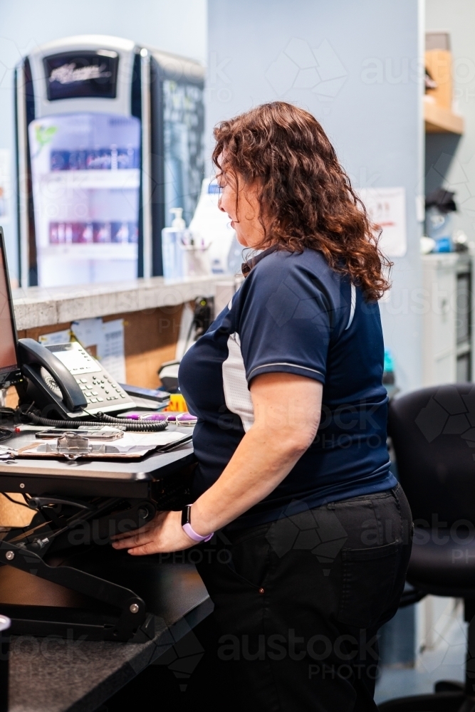 female receptionist working at stand up desk in physio clinic office - Australian Stock Image