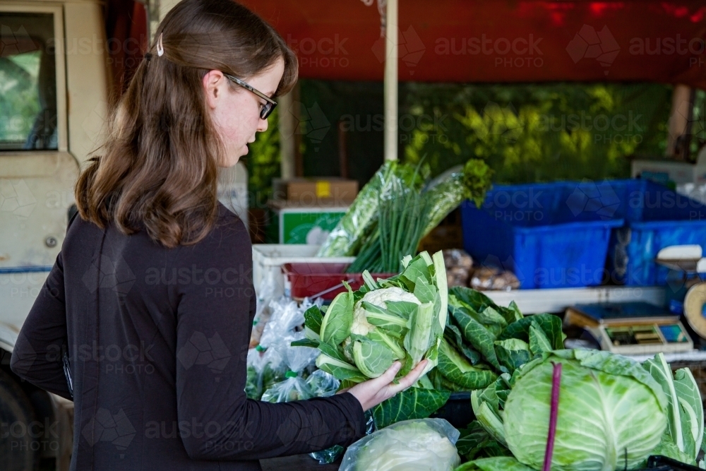 Female shopper looking at cauliflower at farmers market stall - Australian Stock Image