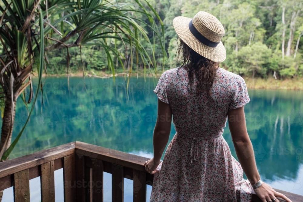 Female sitting in front of blue lake in rainforest setting - Australian Stock Image