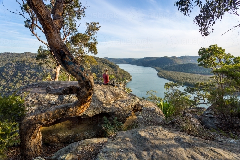 Female sitting on a large rock relaxing in afternoon dappled light the Australian bushland with view - Australian Stock Image