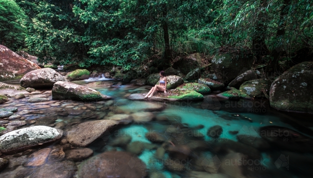 Female sitting on rock at Rainforest swimming hole - Australian Stock Image