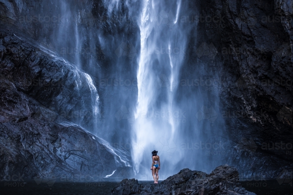 Female standing at the bottom of a giant Waterfall - Australian Stock Image