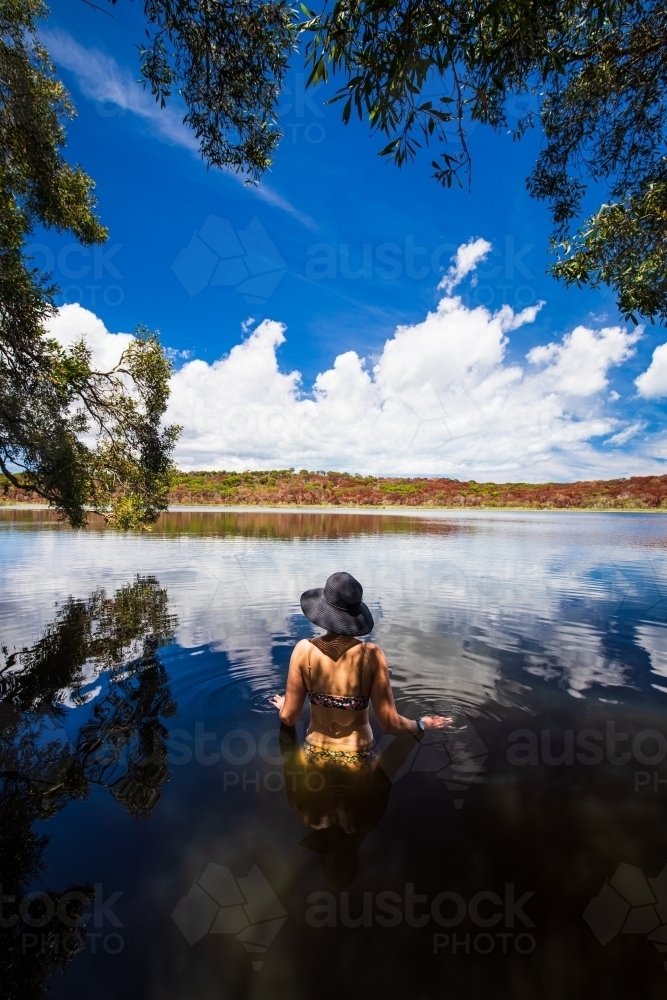 Female standing in the dark reflective water of a lake on Fraser Island - Australian Stock Image