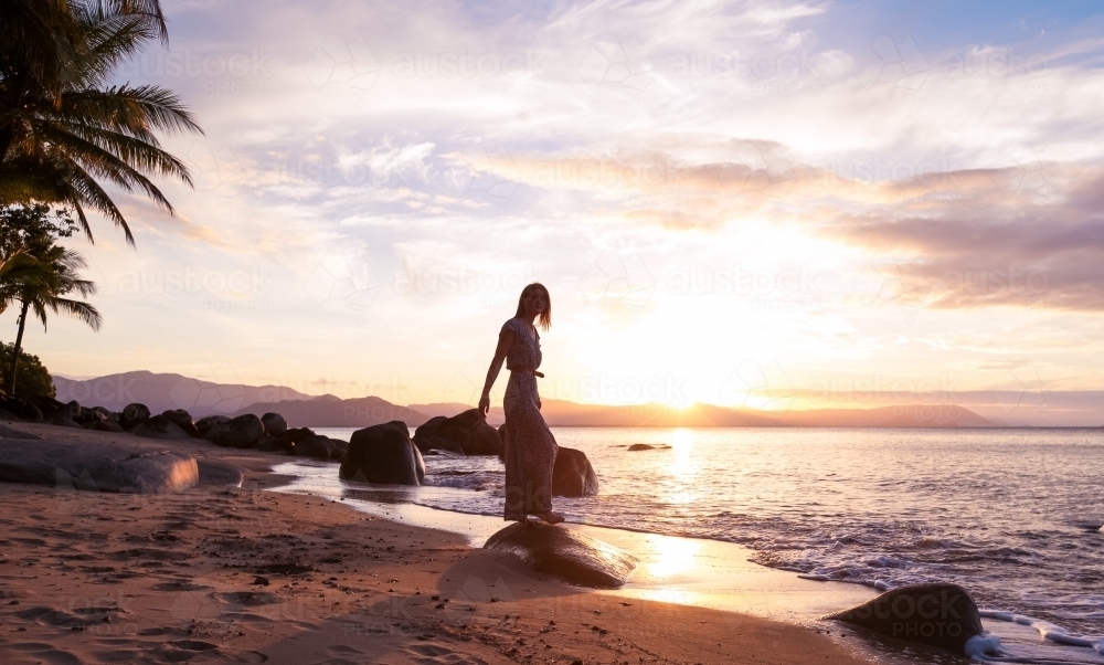 Female standing on rock at the beach with sunset skies - Australian Stock Image