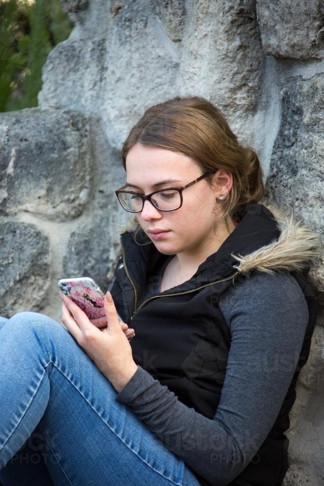 Female student wearing glasses looking at mobile phone - Australian Stock Image