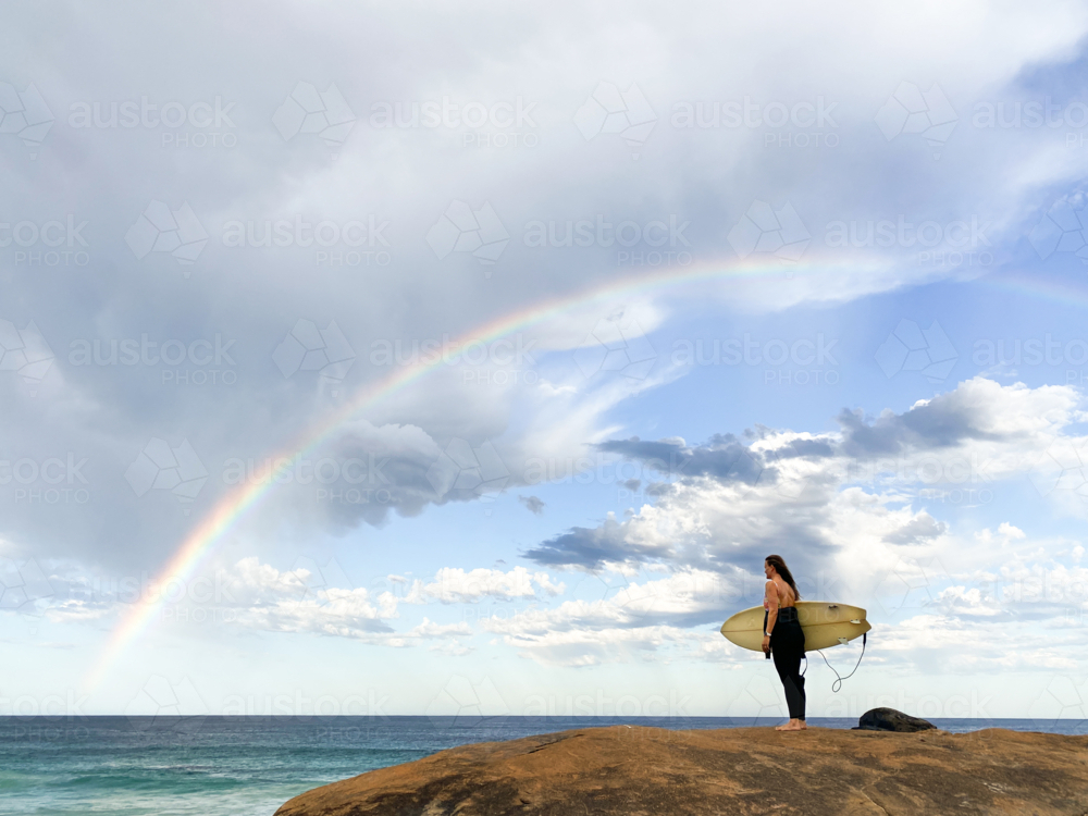 Image of Female surfer holding surfboard looking at sea on rock with ...
