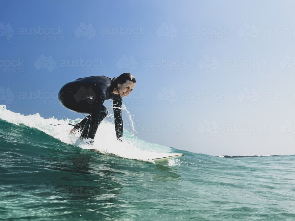 Female surfer mid pop up on surfboard catching green wave - Australian Stock Image
