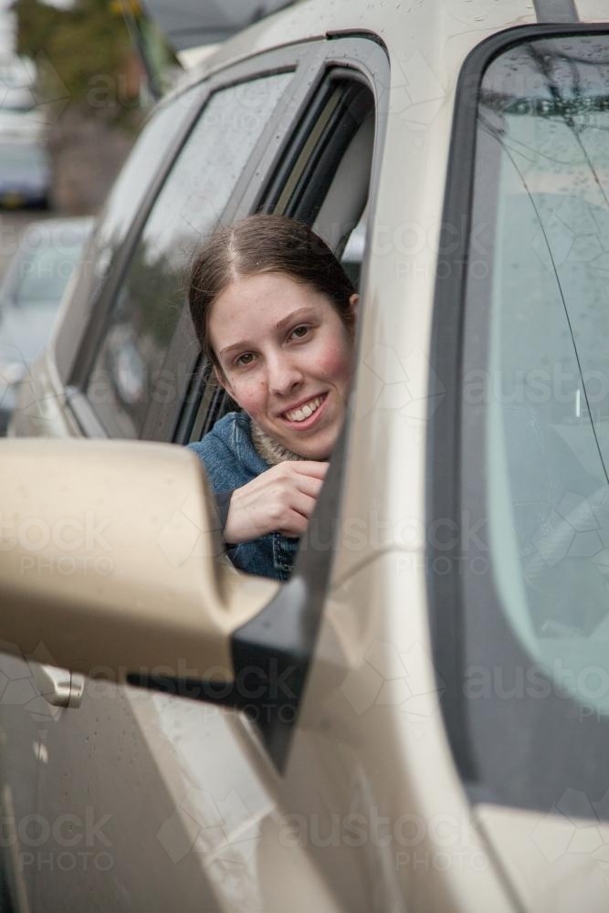 Female teen driver leaning out car window on overcast day - Australian Stock Image