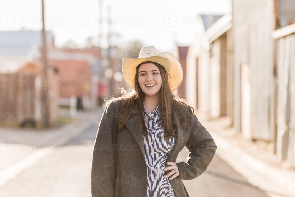Female teen wearing hat standing with hand on hip smiling - Australian Stock Image