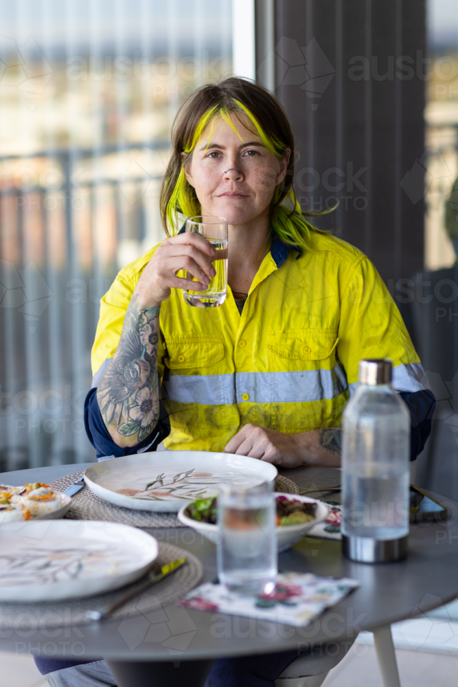 female tradie with bright yellow hair highlights sitting wearing hi-vis clothing at lunch table - Australian Stock Image