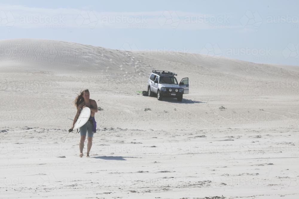 Female walking on sand dunes to head out for a surf - Australian Stock Image