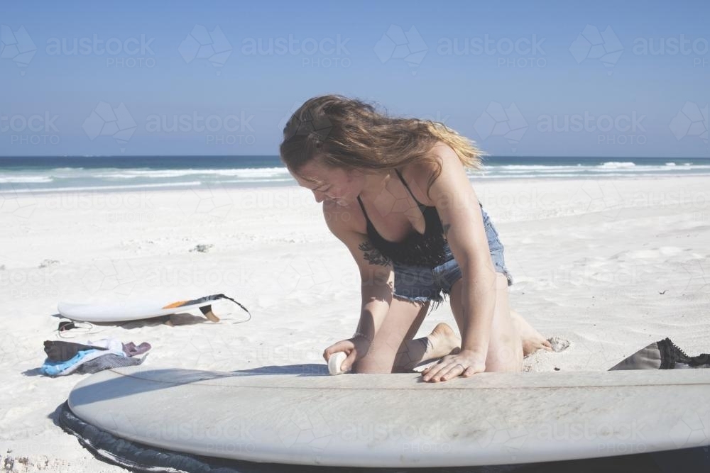 Female waxing surf board pre-surf - Australian Stock Image