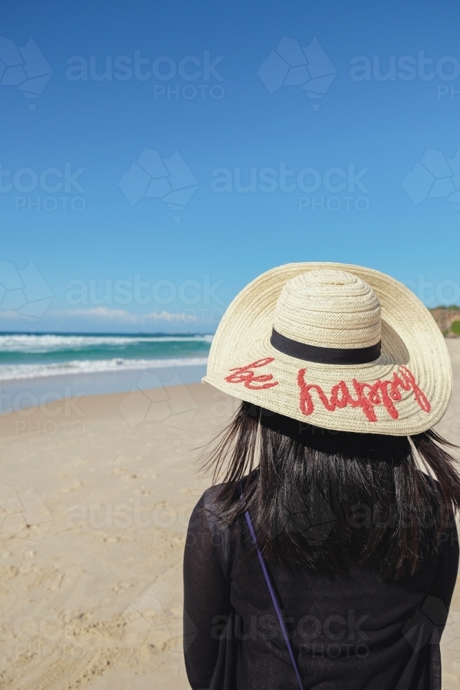 Female wearing be happy hat on the beach - Australian Stock Image