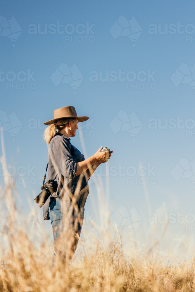 Female with camera over shoulder flying a drone looking to the sky - Australian Stock Image