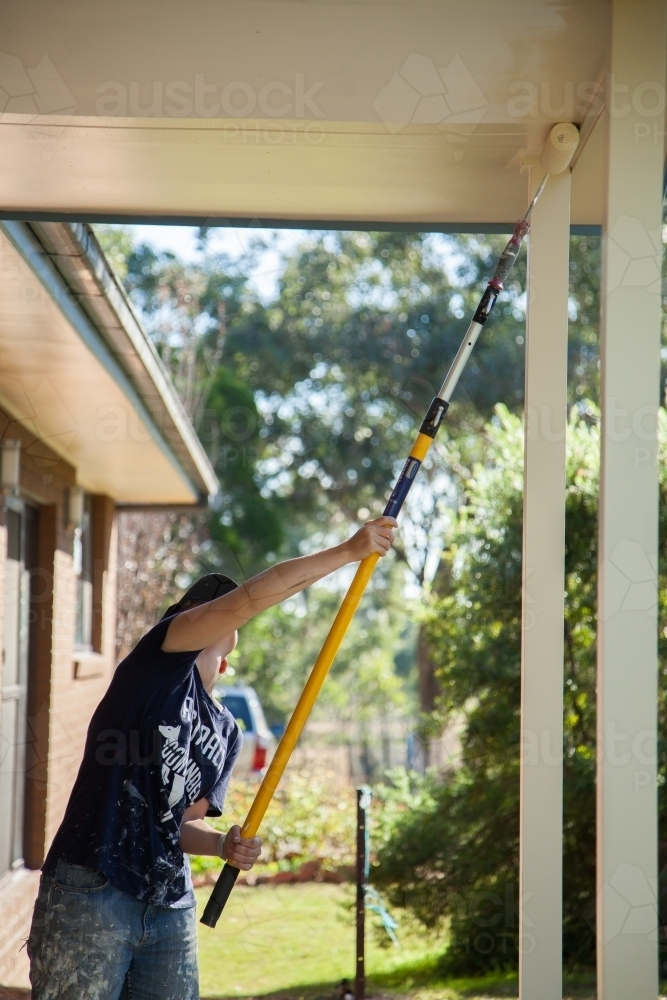 Female worker painting eaves of a home with paint roller - Australian Stock Image