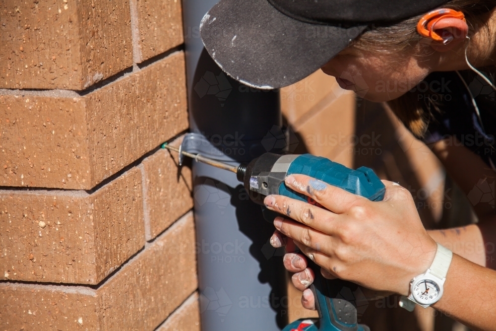 female worker screwing painted downpipe holders onto home - Australian Stock Image