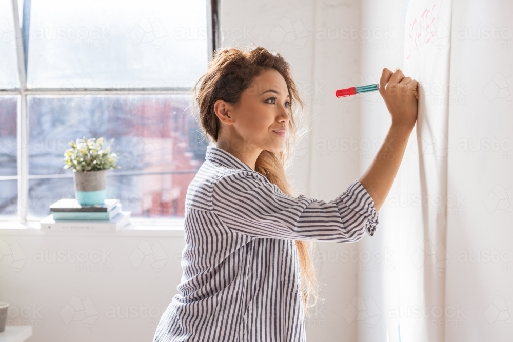 Female writing on butcher's paper on the wall in a studio or classroom - Australian Stock Image