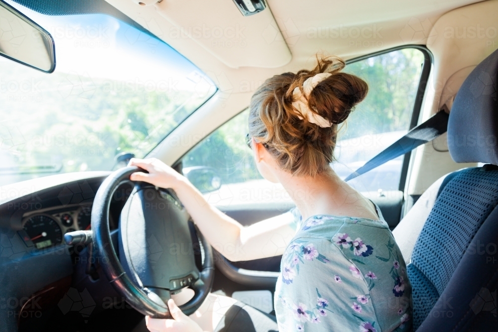 Female young adult driver in car with messy bun hairdo - Australian Stock Image