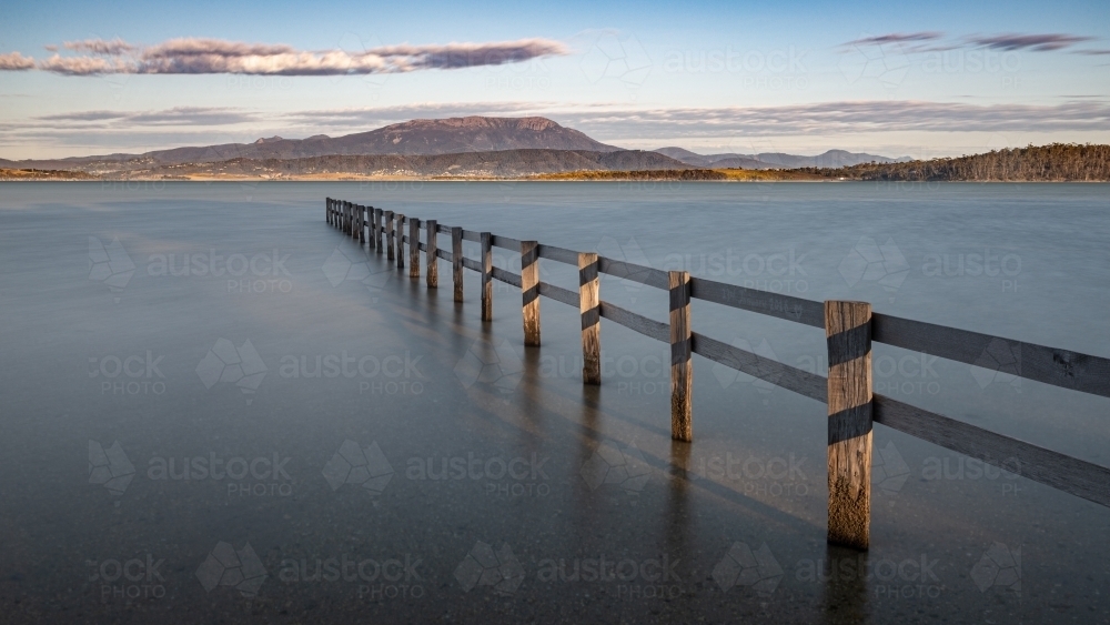 Fence at high tide at Mortimer Bay and Mount Wellington in the background, Tasmania - Australian Stock Image